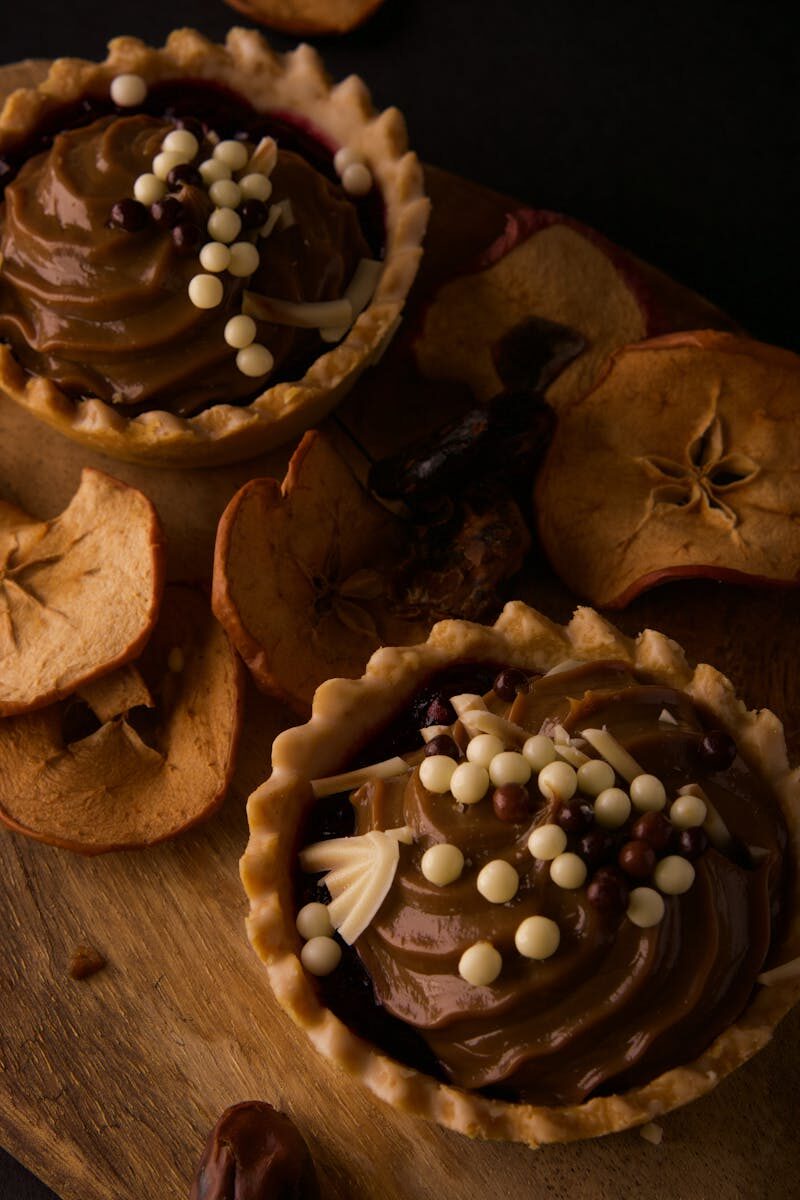 Indulgent chocolate tarts adorned with sprinkles, surrounded by dried apple slices on a rustic cutting board.