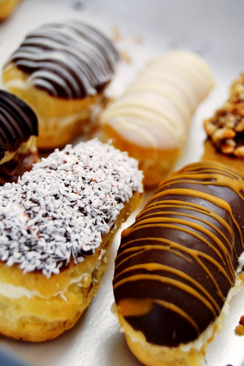 Close-up of assorted eclairs with chocolate, caramel, and coconut toppings.